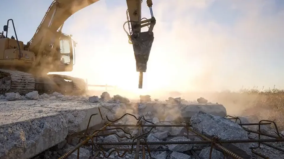 Hydraulic breaker on an excavator splitting a reinforced concrete slab